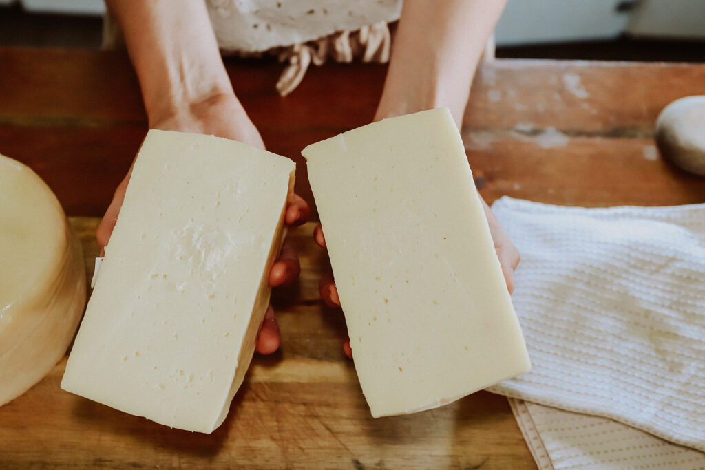 holding a wheel of cheese cut in half in both hands