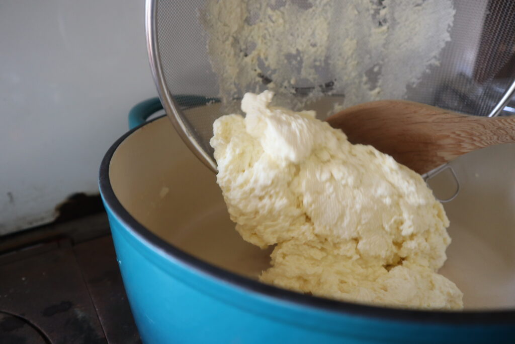 dumping cheese from a fine mesh sieve into a dutch oven