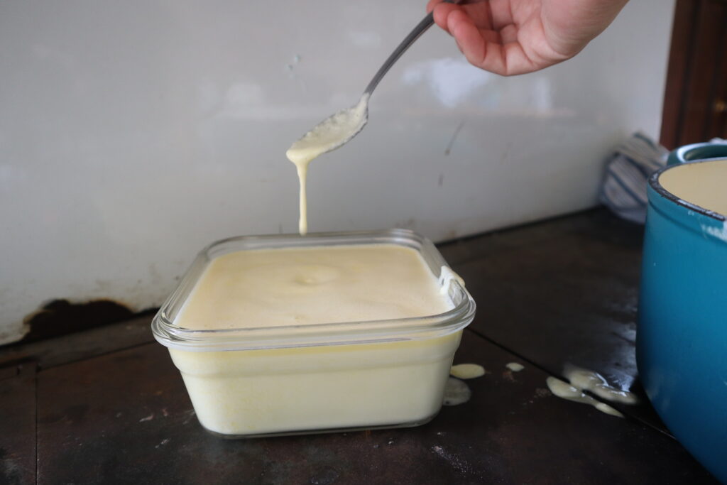 dripping homemade cheese whiz from a spoon into a pyrex bowl 