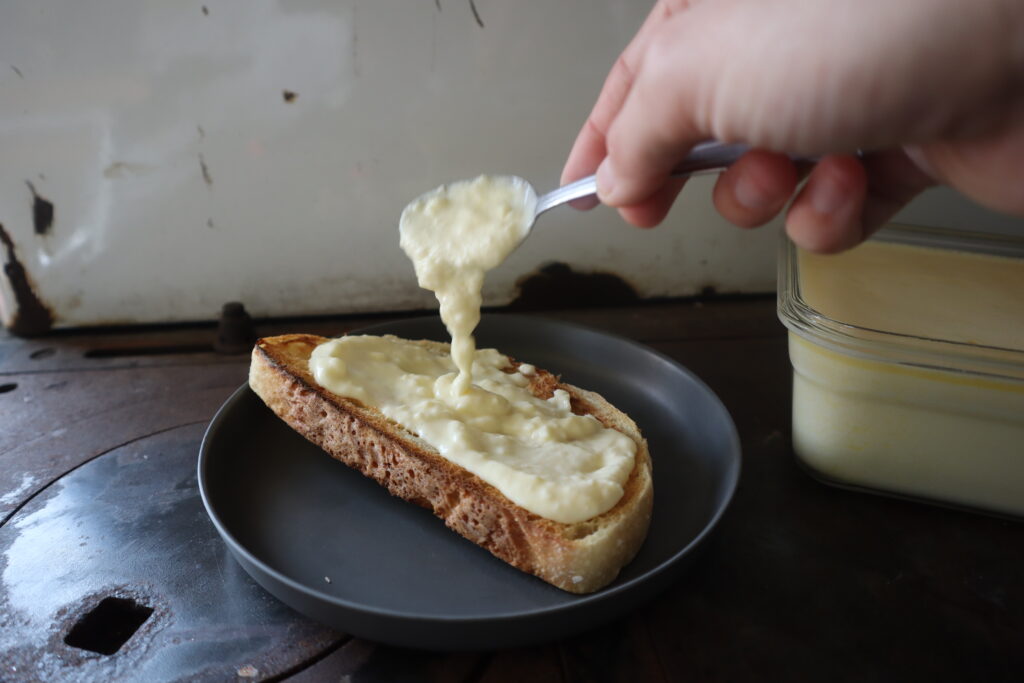 using a spoon to spread homemade cheese whiz on toast 
