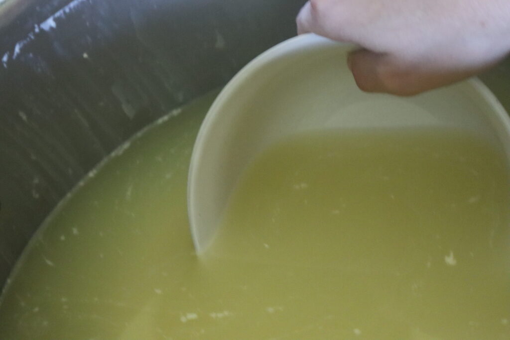 dipping whey out of a pot of cheese