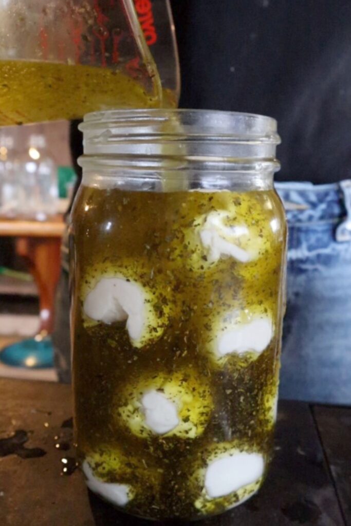 Pouring marinade into a quart jar of cheese and spices 
